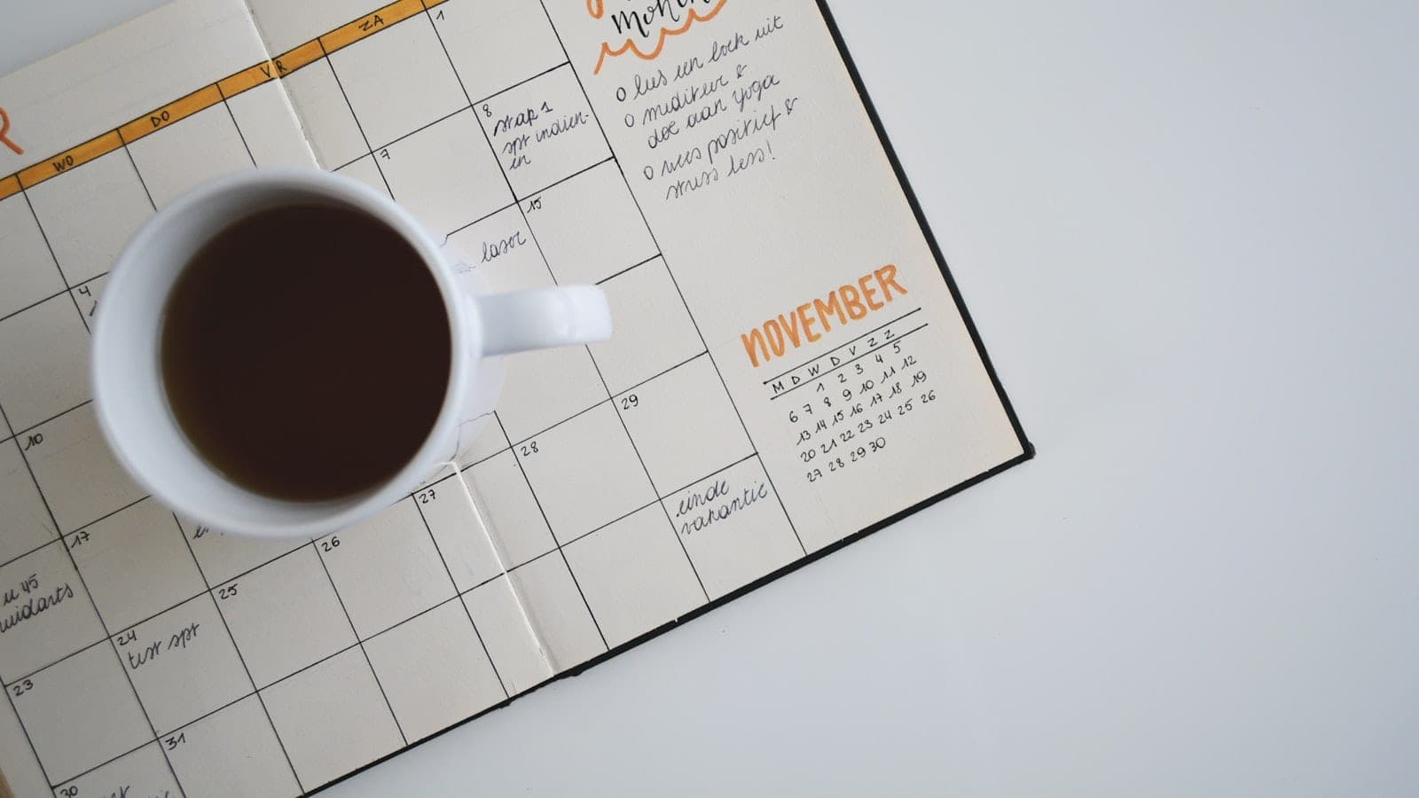 Un bureau en fin de journée avec un carnet ouvert sur une page divisée en sept sections numérotées, un minuteur de cuisine affichant 45 minutes et un écran montrant un agenda hebdomadaire.