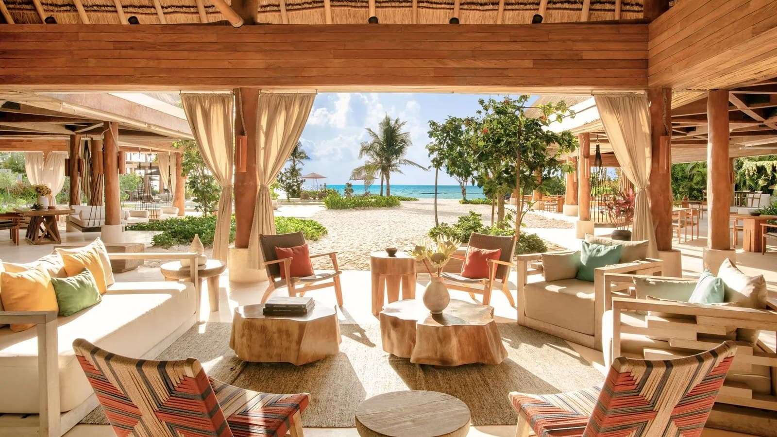 Salon ouvert en bois du Rosewood Mayakoba, la mer des Caraïbes en arrière-plan
