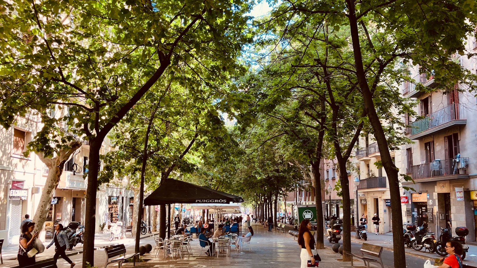 Vue plongeante sur un croisement en damier de l’Eixample à Barcelone en fin de matinée, taxis noir et jaune arrêtés au feu et terrasses de café sur les angles coupés.
