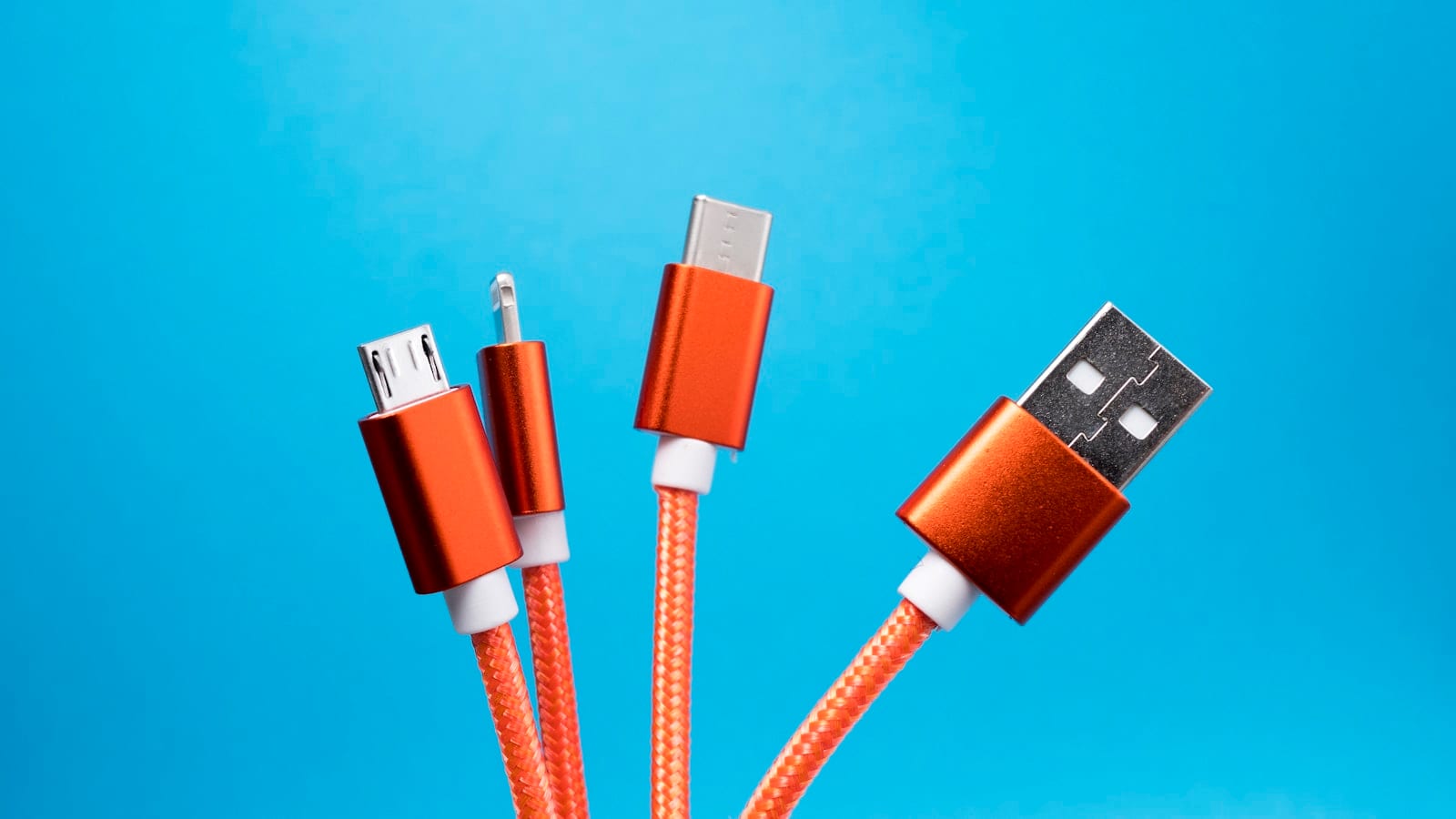 Sept chargeurs GaN multiports alignés sur un plan de travail gris, reliés à un wattmètre USB-C à écran couleur, avec un ordinateur portable et un téléphone en charge.
