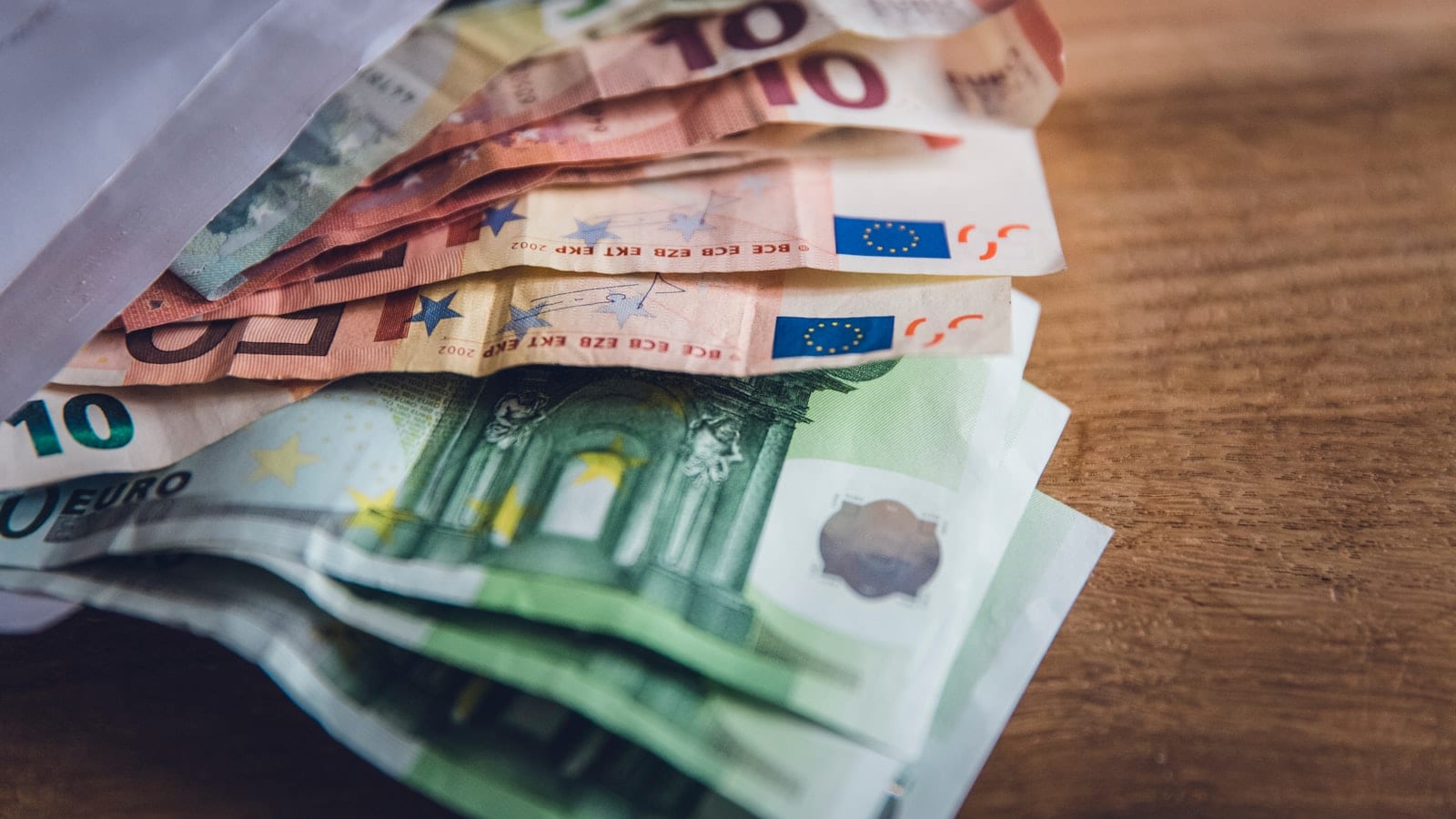 Relevés bancaires annotés au surligneur posés sur un bureau, à côté d'un ordinateur portable affichant un tableur de dépenses logicielles et d'une calculatrice.