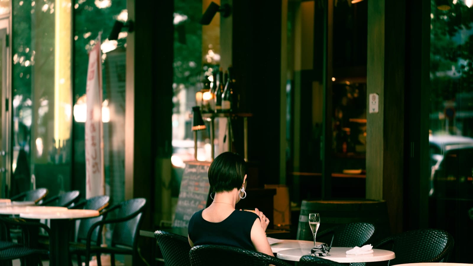 Salle de restaurant parisienne en soirée, tables dressées avec nappes blanches, serveur prenant une commande auprès de quatre convives en tenue de bureau
