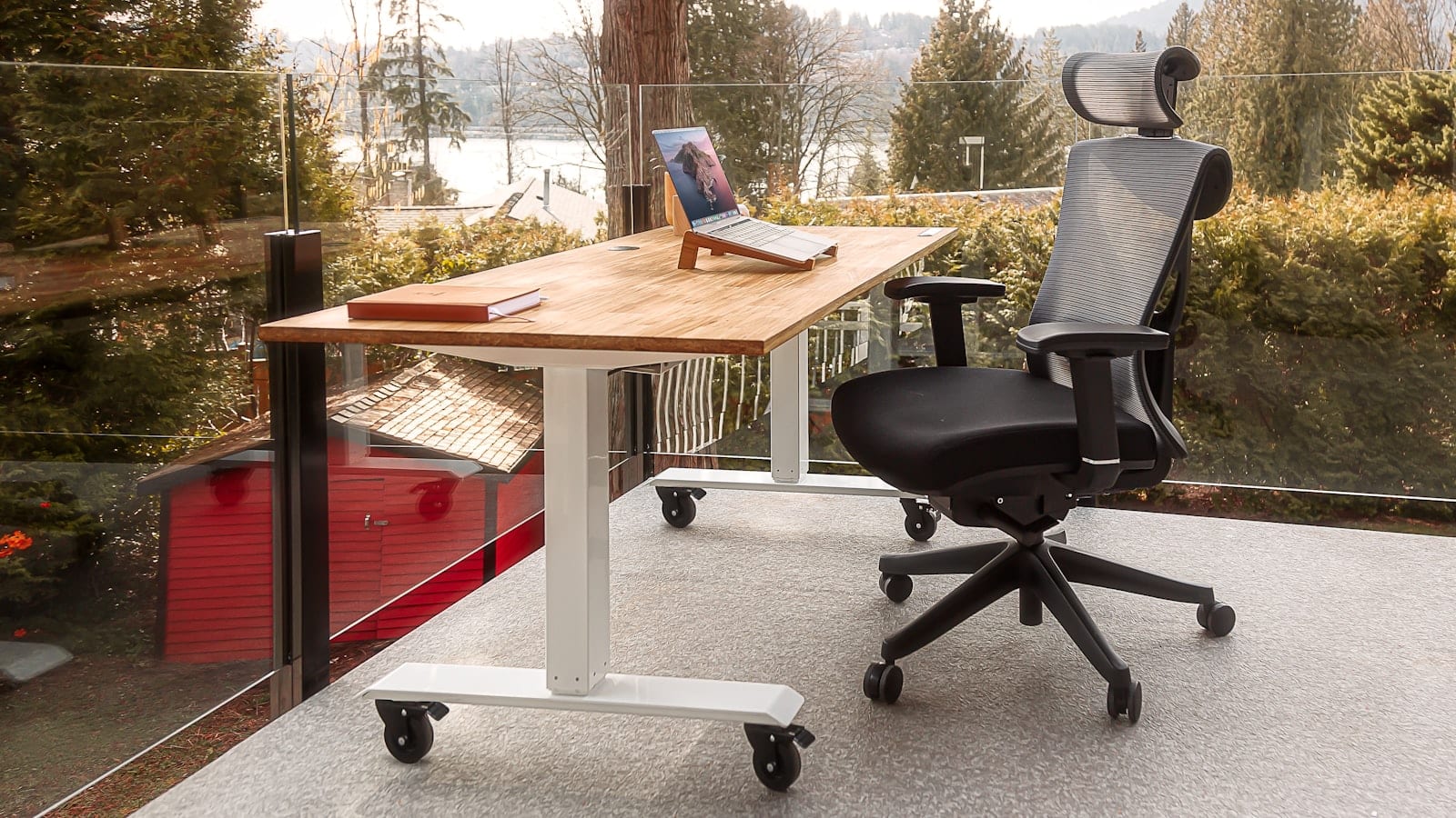 Fauteuil de bureau en maille noire vu de trois quarts devant un bureau en bois clair, accoudoirs réglés en position basse