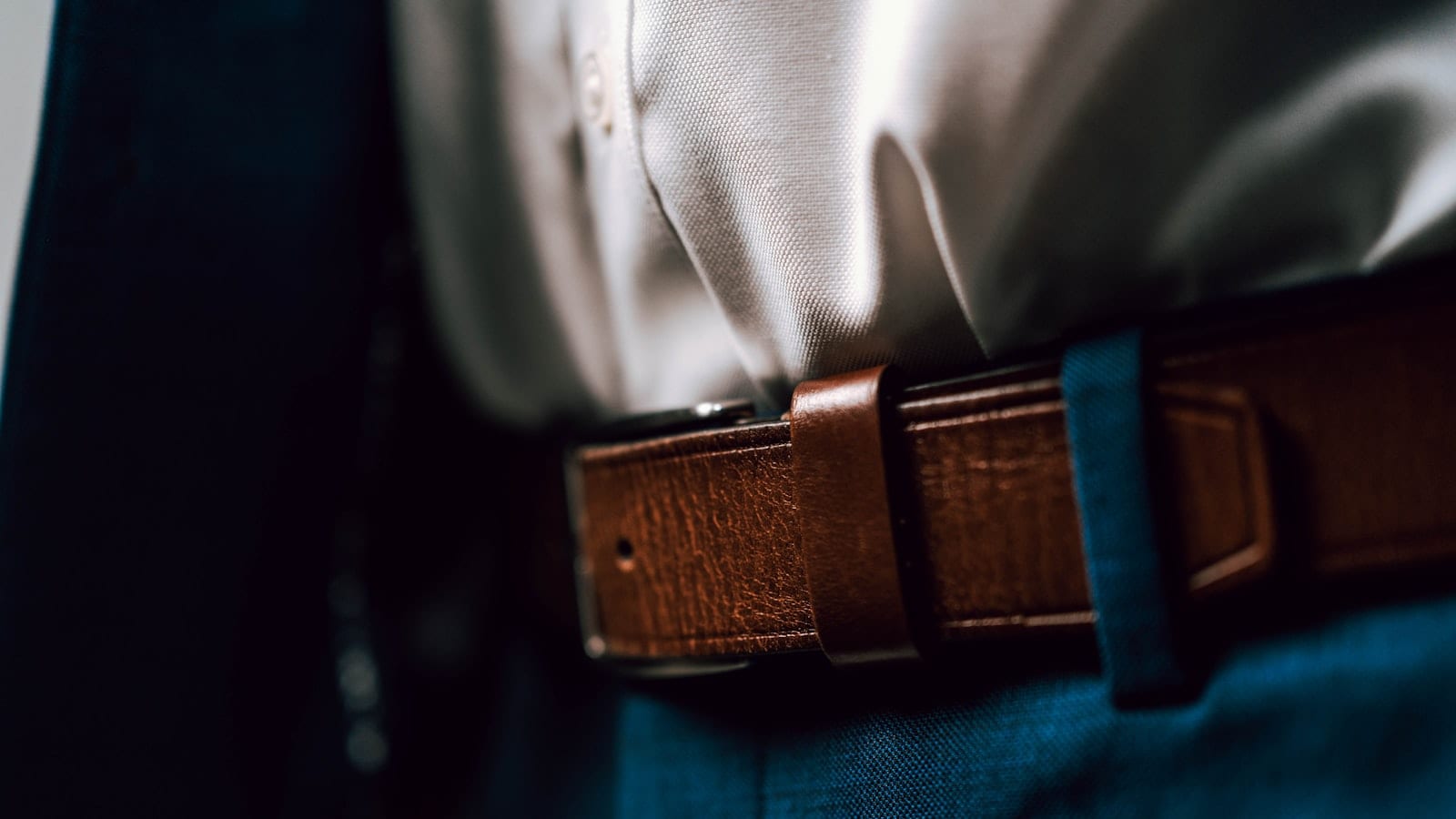 Cinq pantalons de couleur sombre posés à plat côte à côte sur une table en bois clair, avec une étiquette numérotée sur chaque ceinture