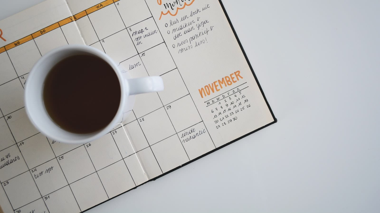 Un bureau en fin de journée avec un carnet ouvert sur une page divisée en sept sections numérotées, un minuteur de cuisine affichant 45 minutes et un écran montrant un agenda hebdomadaire.