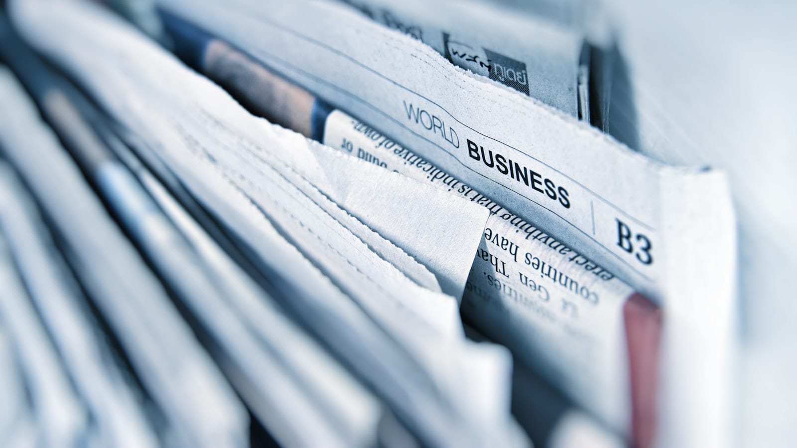 Écran d'ordinateur affichant un briefing de veille en deux colonnes, avec une liste de sources numérotées à gauche et un résumé structuré à droite, posé sur un bureau avec un carnet ouvert.