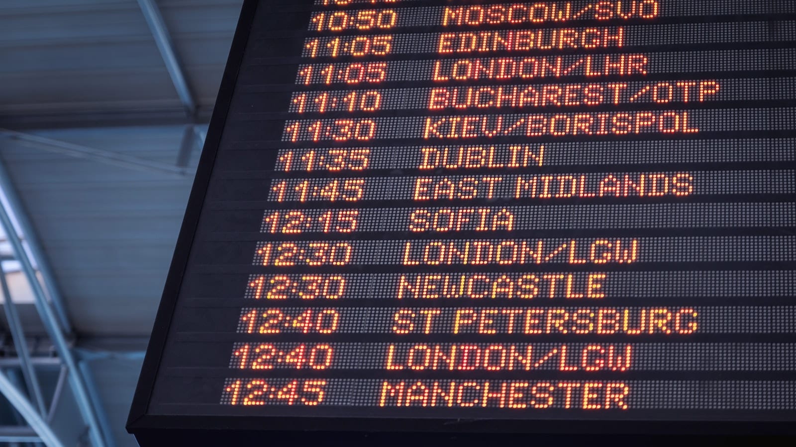 Écran d'affichage d'aéroport indiquant plusieurs vols retardés, avec un voyageur consultant son téléphone au premier plan